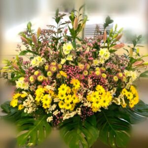 Centro de flores doble con flores variadas en tonos amarillos principalmente.