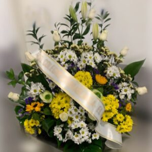 Centro de flores funerarias en abanico con margaritas blancas y amarillas, rosas blancas y otras flores varias