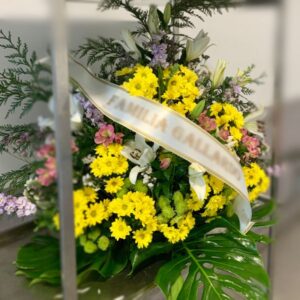 Centro de flores funerarias en abanico con tonos amarillos salpicados de otras flores de distintos colores